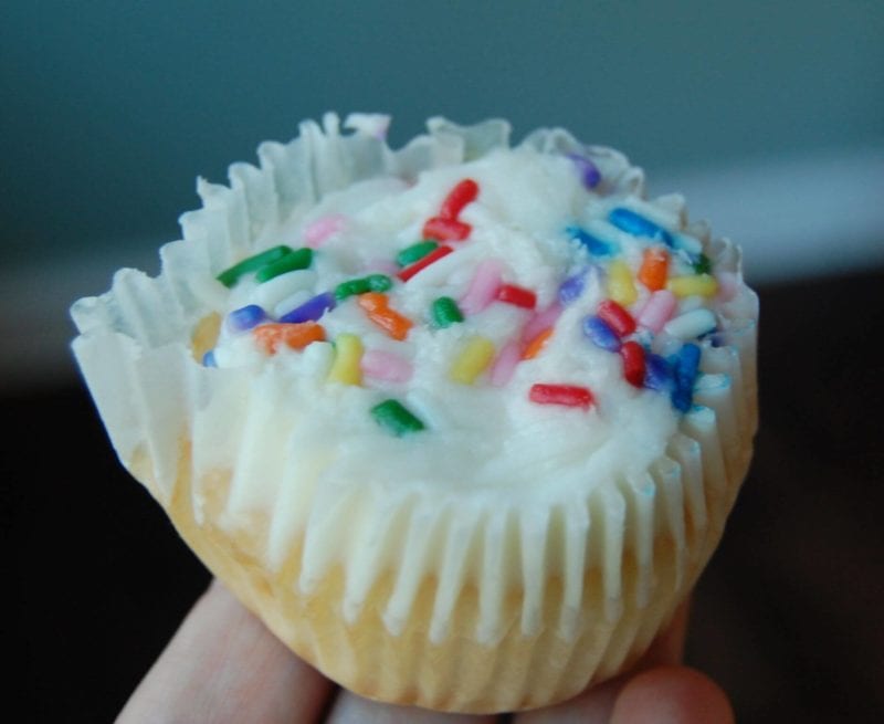 A vanilla cupcake with vanilla frosting and colorful sprinkles. 