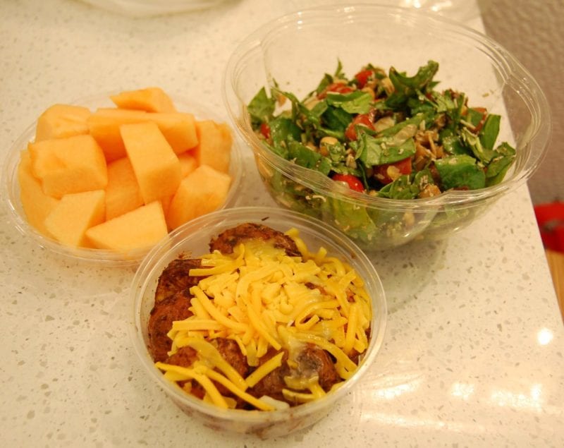A hearty salad, cantaloupe, and roasted potatoes topped with grated cheese packed in containers from Toasties deli in NYC. 
