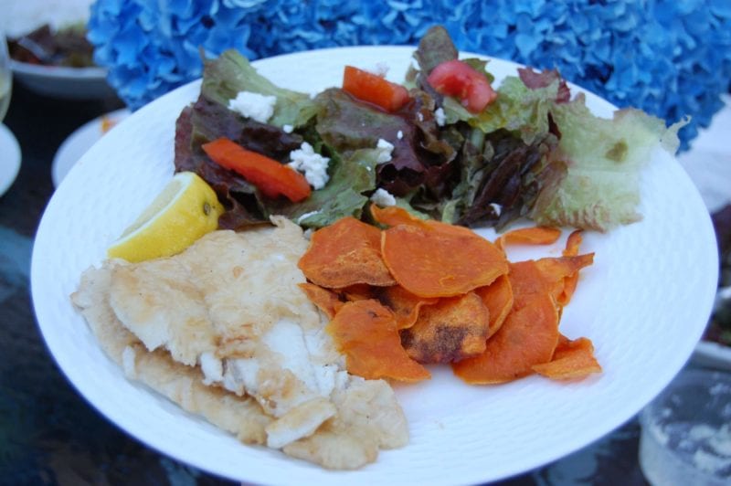 Baked sweet potato chips, sautéed fish, and a salad on a plate. 