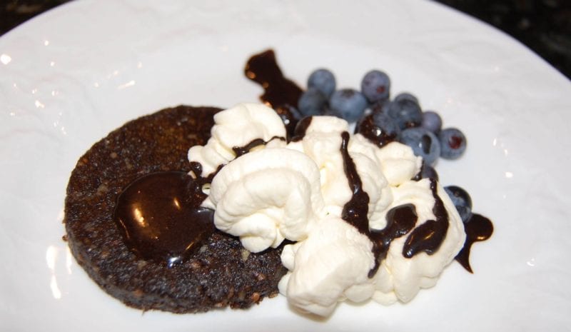 An individual chocolate torte topped with whipped cream, chocolate sauce, and blueberries. 