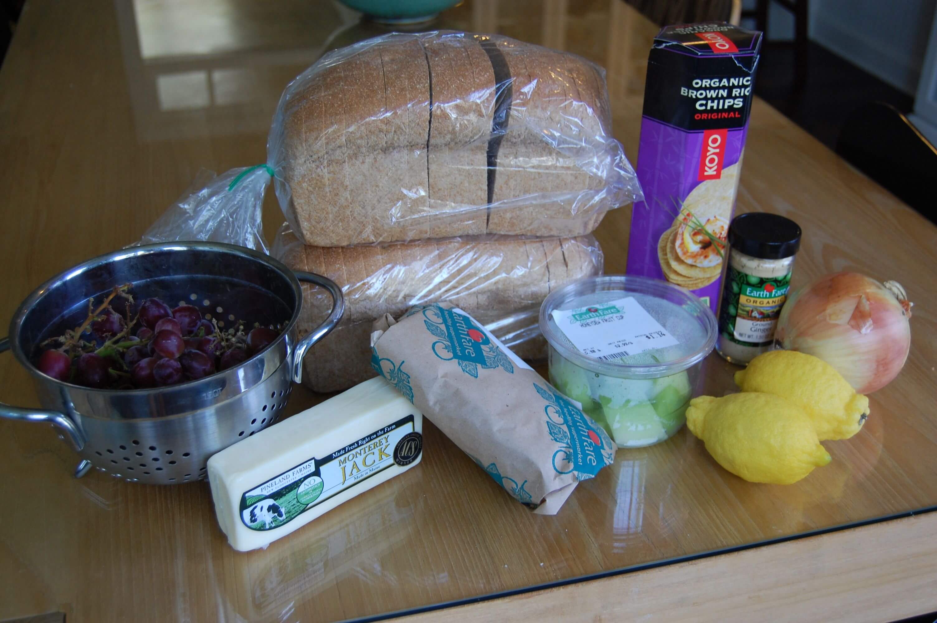 Groceries from Earthfare that include flounder, an onion, lemons, honeydew, grapes, cheese, whole-wheat bread, brown rice crackers, and ground ginger. 