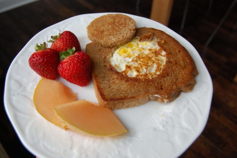 Whole-wheat toast with egg fried in the middle with a side of strawberries and cantaloupe. 