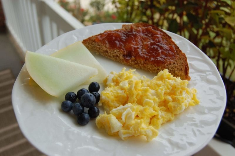 Scrambled eggs, toast with jelly, and fruit on a plate. 
