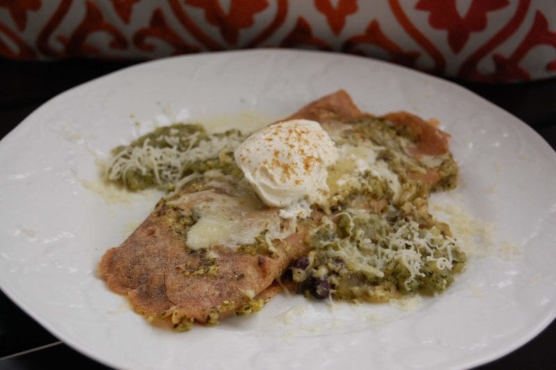 Vegetarian enchilada dish topped with homemade tomatillo salsa and cheese on a plate.