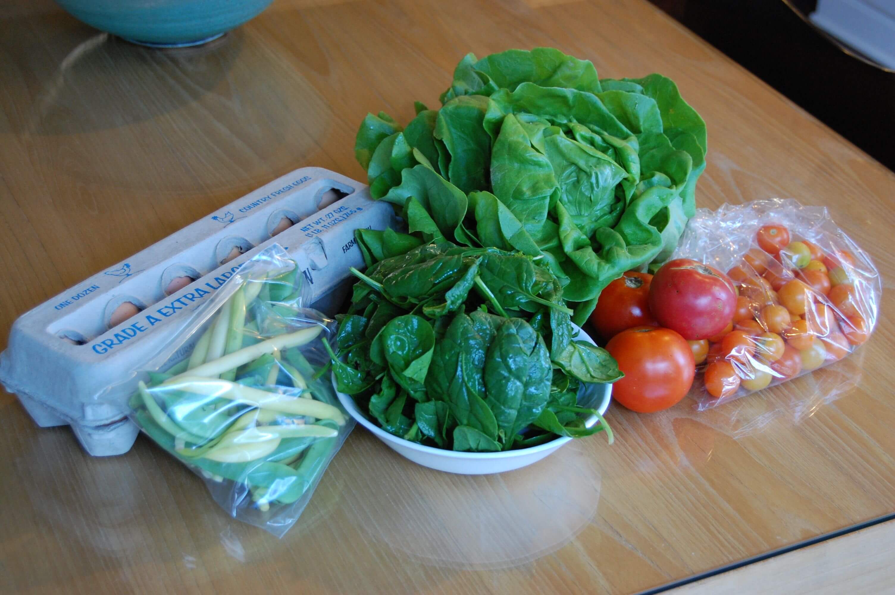 Fresh produce from the farmers market that includes eggs, lettuce, spinach, tomatoes, and green beans. 