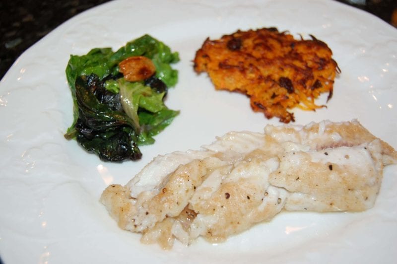 White fish with a side of sweet potato pancakes and greens on a plate. 