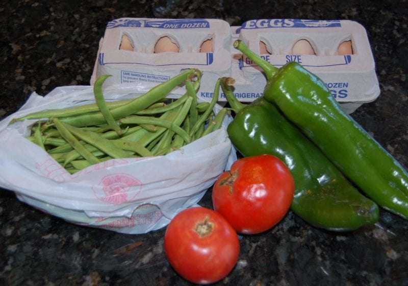 Groceries that include green beans, tomatoes, peppers, and eggs. 