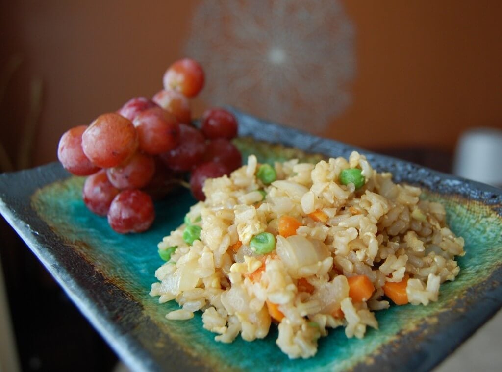 Homemade fried rice and a side of grapes on a plate. 