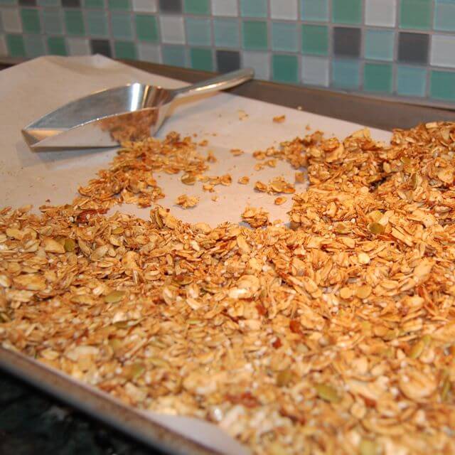 recipe for homemade granola on a baking tray with a stainless steel scoop