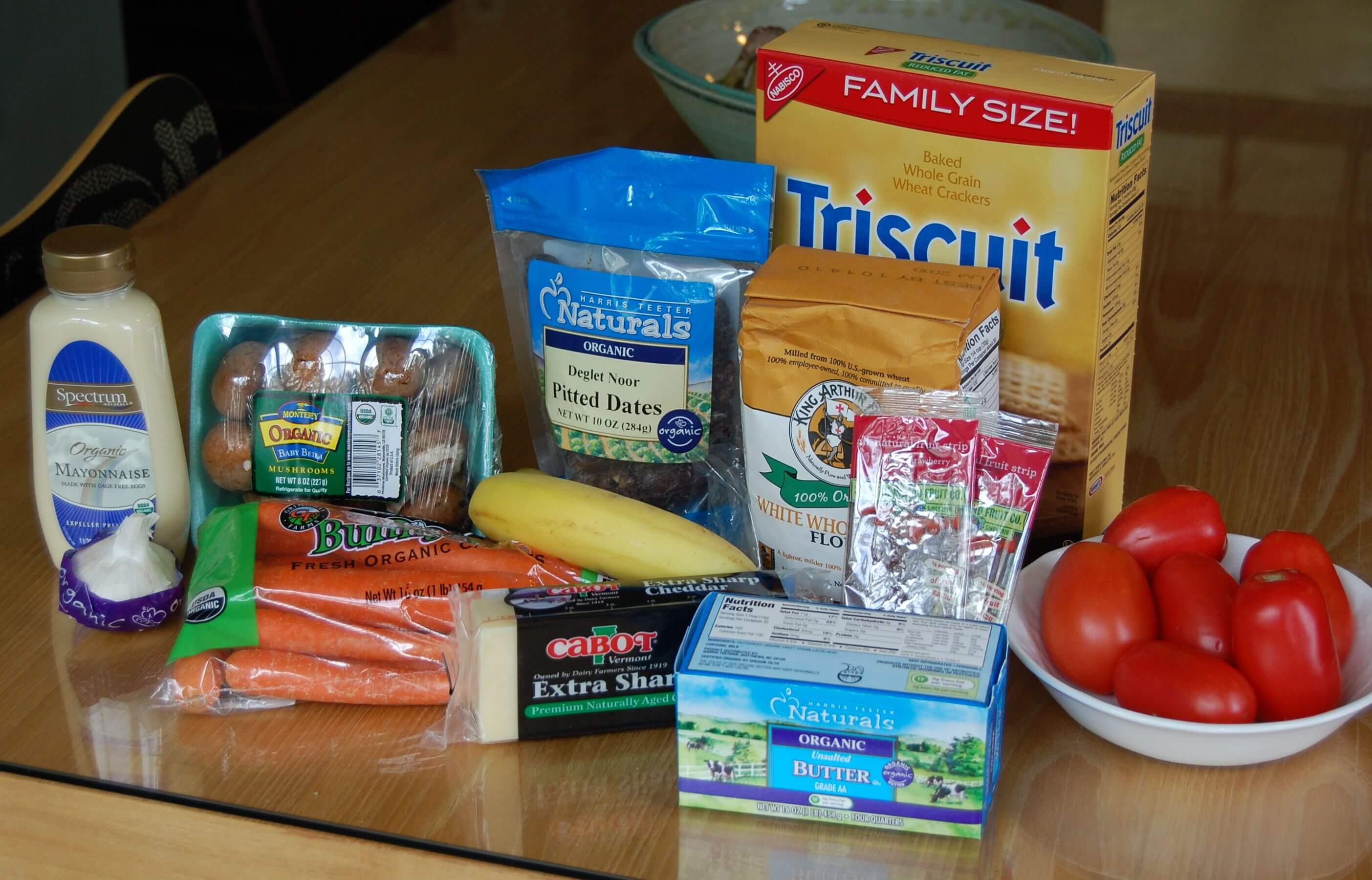 Groceries from Harris Teether that includes mayonnaise, Triscuits, dates, bananas, tomatoes, mushrooms, carrots, garlic, and cheese. 