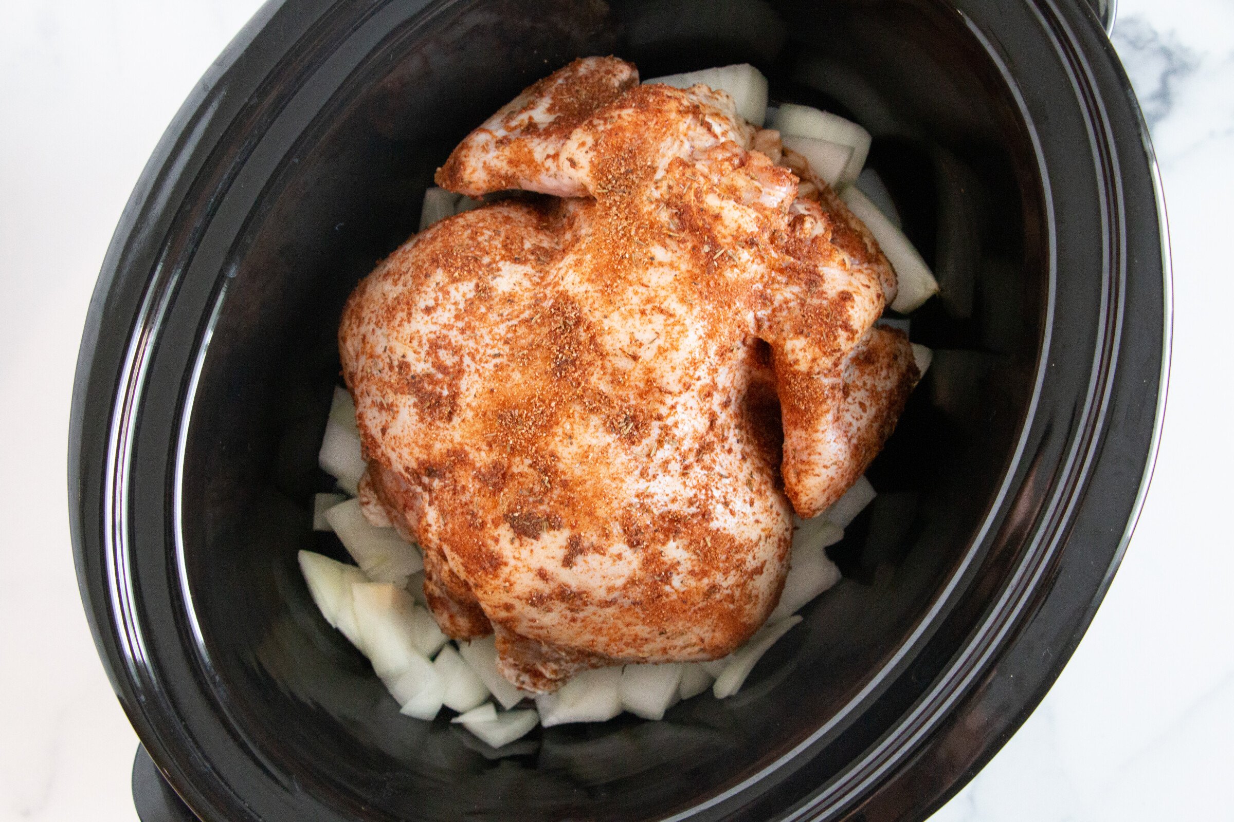 Whole chicken inside a slow cooker on a bed of chopped onions