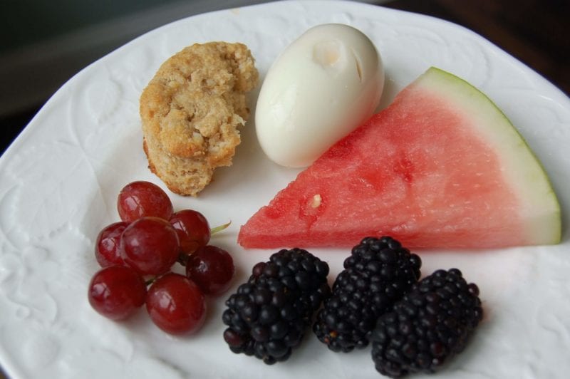 Slice of watermelon, grapes, blackberries, hard boiled egg, and a cheese biscuit on a plate. 