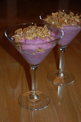 A berry smoothie in a martini glass topped with granola. 