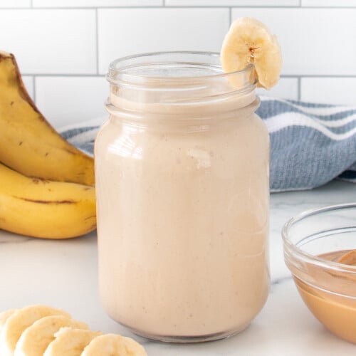 A Peanut Butter Banana Smoothie in a mason jar with a banana slice on the side.