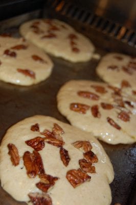 Banana pancakes with pecans in them cooking on the stove. 