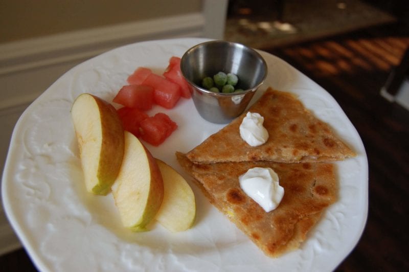 Homemade cheese and corn quesadillas with a side of fruit and frozen peas on a plate. 