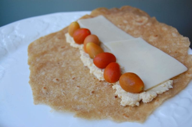 Homemade whole-wheat tortillas with hummus, cheddar cheese, and tomatoes on a plate.