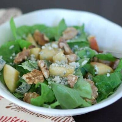 large white bowl filled with greens, apple chunks, walnuts, and cheese