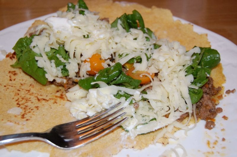 Homemade ground pork tacos with cheese, tomatoes, and greens on a tortilla. 